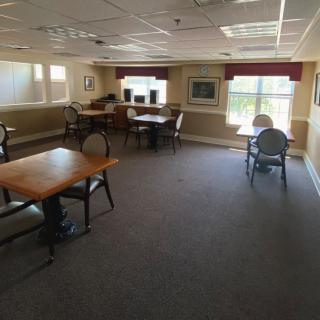 A spacious room with several tables and chairs, featuring large windows and carpeted floors.