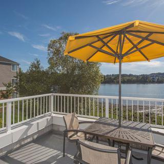 A patio with a yellow umbrella overlooking a lake on a sunny day.