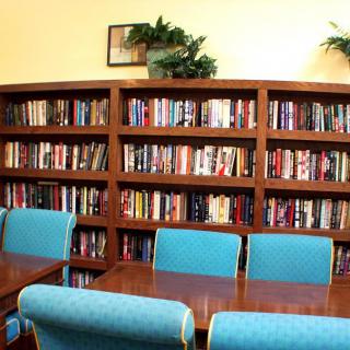 A cozy library room with bookshelves filled with books and blue chairs around a wooden table.