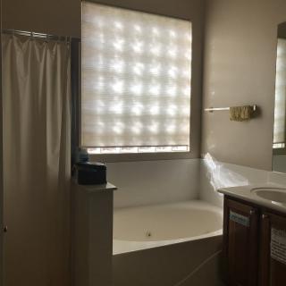 A bathroom with a large bathtub, shower curtain, and a window illuminating the space.