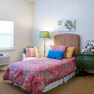 A cozy bedroom with a colorful bedspread, white chair, and green bedside table.