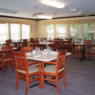An empty dining room with neatly arranged tables and chairs, well-lit by natural light from the windows.