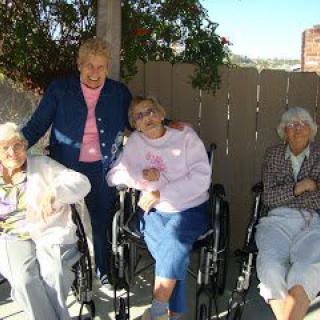A group of elderly friends enjoy a sunny day outdoors, with some sitting in wheelchairs.