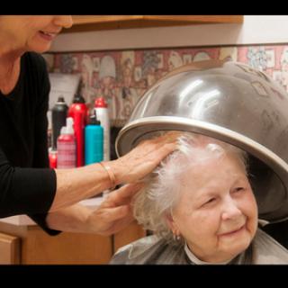An elderly woman enjoying a hair treatment at a salon, under a heated dryer.