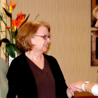 Two women engaged in conversation indoors near a floral arrangement.