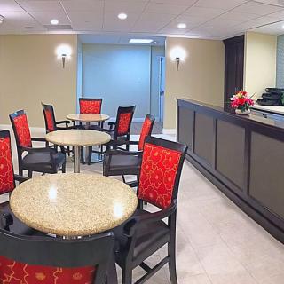 A well-lit lobby with red and black chairs, round tables, and a reception desk.