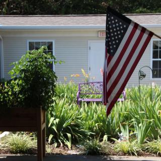 A front yard with a garden featuring an American flag and various plants, in front of a house.