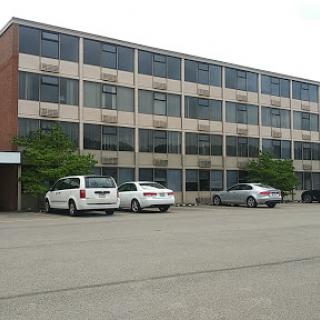 A modern multi-story building with a parking lot in front.