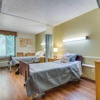 A hospital room with two patient beds, featuring simple furnishings and bright lighting.