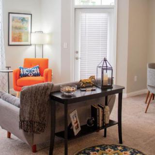 A cozy, modern living room featuring an orange chair, a lamp, and a small bookshelf with decorative items.