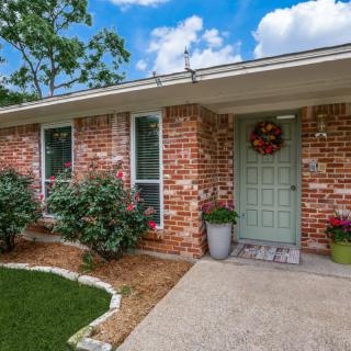 A cozy brick house with a welcoming front entrance adorned with potted plants and a wreath on the door.