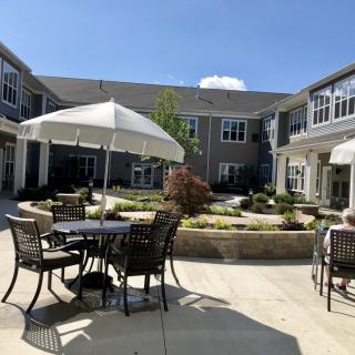 A sunny courtyard with outdoor seating, featuring tables and umbrellas amidst pleasant landscaping.