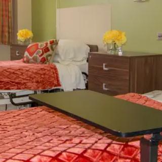 A well-decorated bedroom with two beds, each adorned with orange quilts and decorative pillows. Yellow flowers sit on nightstands beside each bed.