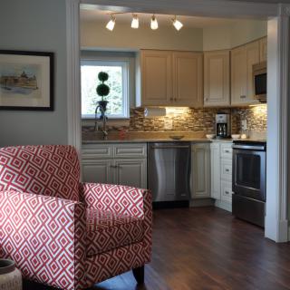A modern kitchen with stainless steel appliances and an adjacent living area featuring a patterned armchair.