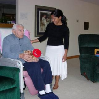 A caregiver attends to an elderly man in a nursing home setting.