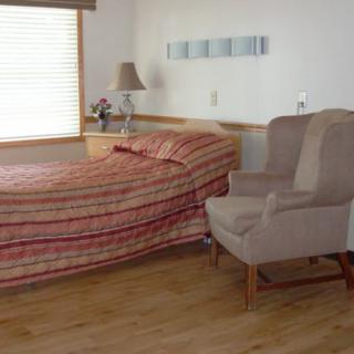 A cozy bedroom featuring a bed with striped bedding, an armchair, and a window letting in natural light.