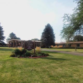 A picturesque view of a building surrounded by lush green grass and trees, featuring a decorative sign in the foreground.