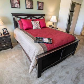 A cozy bedroom with a neatly made bed featuring red and beige bedding, flanked by nightstands with lamps, and decorated with framed artwork on the wall.