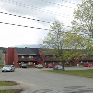 A residential building with a parking lot and several cars under an overcast sky.