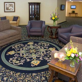 A cozy living room with sofas and armchairs arranged around a circular carpet, featuring a floral arrangement on a coffee table.