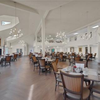 A spacious and bright dining room with neatly arranged tables and chairs, illuminated by elegant chandeliers.