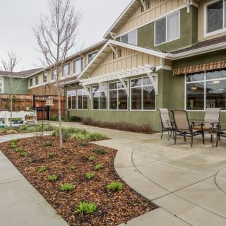 A well-maintained garden area with a paved pathway and patio furniture, adjacent to a two-story building.