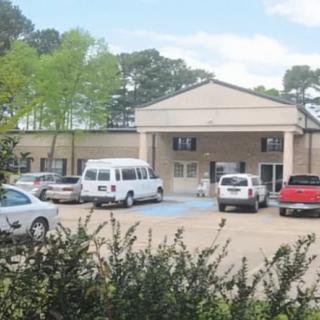 A building with a parking lot in front, featuring several cars and a van.