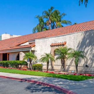 A suburban house with a red-tiled roof and palm trees in front, under a clear blue sky.