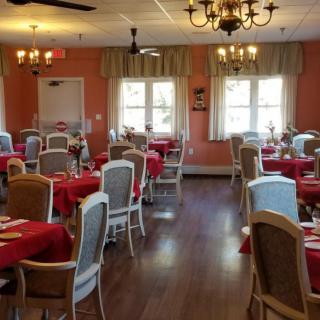 A cozy dining room featuring multiple tables with red tablecloths and a classic decor style.