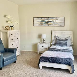 A cozy bedroom with a single bed, armchair, and dresser, complemented by wall art and decor.