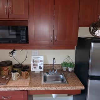 A compact kitchenette with a microwave, sink, and various kitchenware on the countertop.