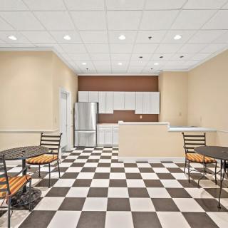A modern kitchen or cafe interior with checkered flooring, white cabinets, and several tables and chairs.
