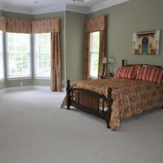 A spacious bedroom with a wooden bed, large windows, and elegant curtains.