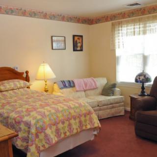 A cozy bedroom with a bed, sofa, and armchair, featuring soft lighting and decorative elements.