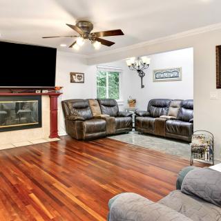 A cozy living room featuring a hardwood floor, comfortable sofas, a fireplace, and a ceiling fan.