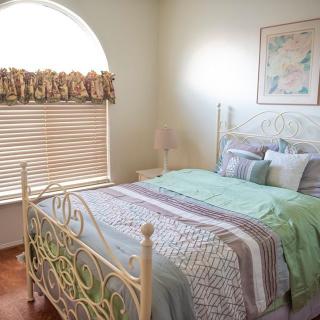 A cozy bedroom with a neatly made bed, window with blinds and curtains, and wall art.