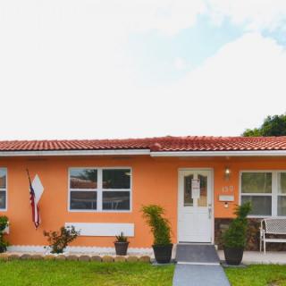 A small orange house with a well-kept lawn and potted plants in front.