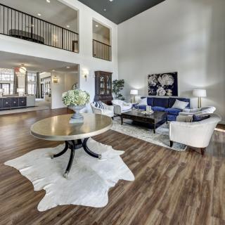 A spacious and modern living room with high ceilings and wood flooring, featuring elegant furniture and abundant natural light.