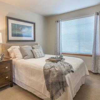 A cozy and elegantly decorated bedroom with a neatly made bed, wooden nightstand, and large window for natural light.