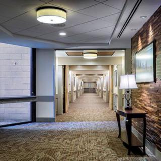 A modern hotel corridor featuring carpeted floors, wall lamps, and framed artwork.