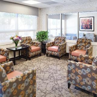 A well-lit waiting room with patterned chairs and a carpet, adorned with floral decorations.