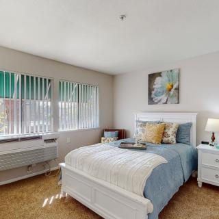 A cozy bedroom with a neatly made bed, nightstands, and large windows allowing natural light.