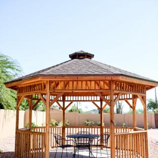 A wooden gazebo in a sunny backyard setting.