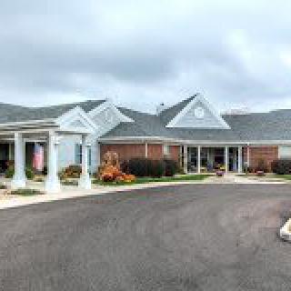 An exterior view of a building with a driveway and landscaped entrance under a cloudy sky.