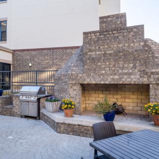 An outdoor patio features a large stone fireplace, a barbecue grill, and seating with potted plants for decoration.