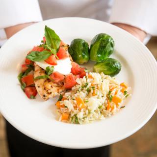 A gourmet dish featuring salmon topped with tomatoes and basil, served with rice and Brussels sprouts.