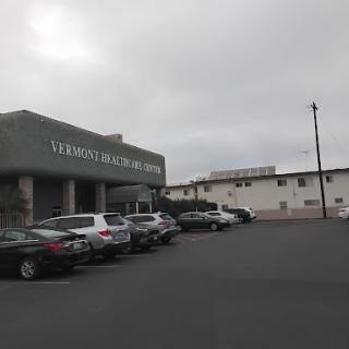 A view of a medical facility with a parking lot under a cloudy sky.