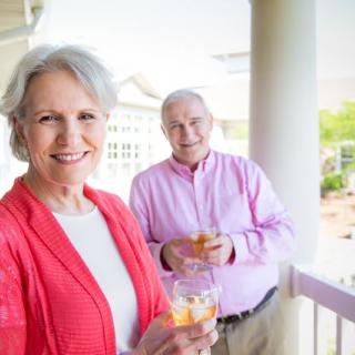 An elderly couple enjoying drinks on a porch.