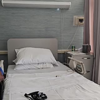 A view of a hospital patient room, featuring a neatly made bed and basic medical equipment.