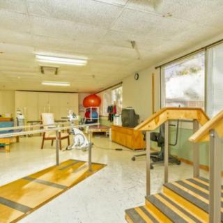 A spacious office area featuring desks, chairs, and a staircase with large windows allowing natural light.